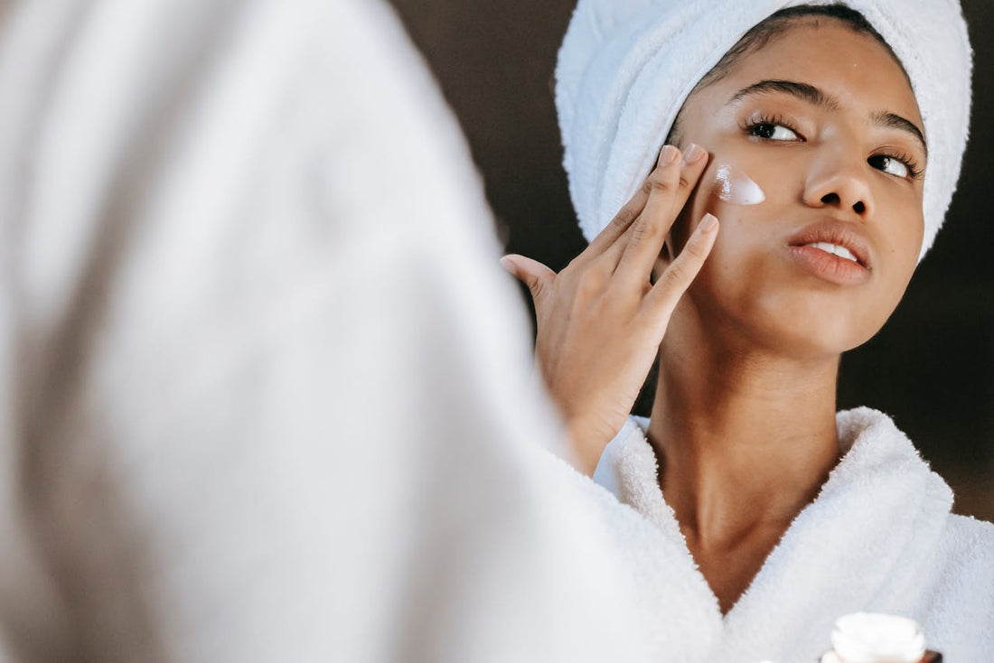 a woman in a white robe and towel applying face cream