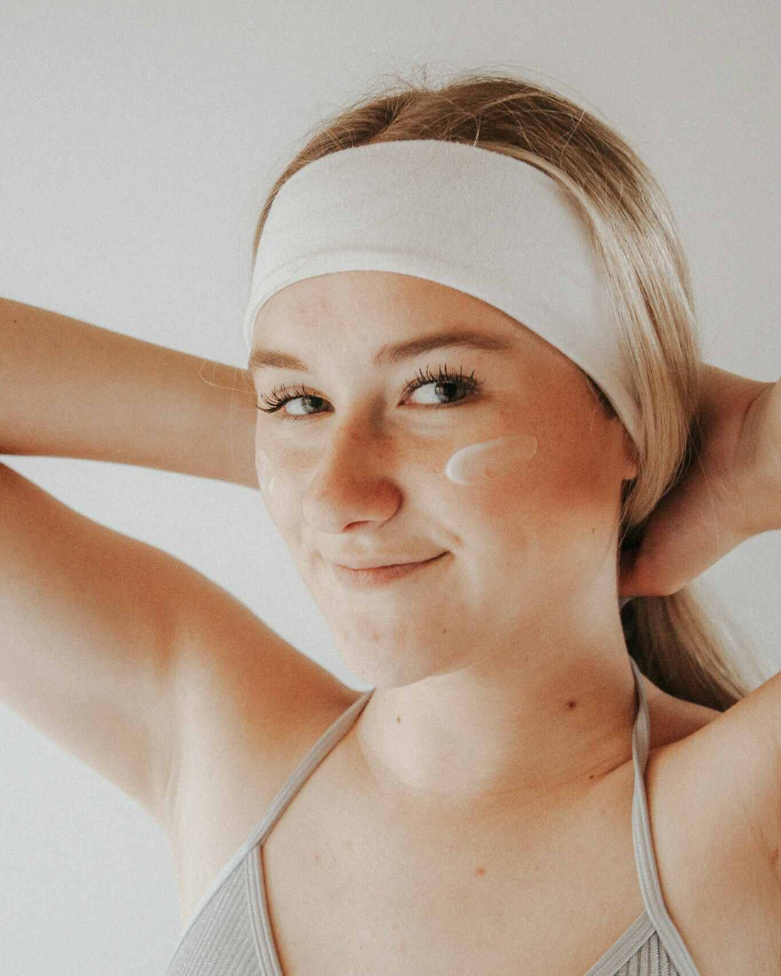 a woman in a white headband with moisturizer on her face